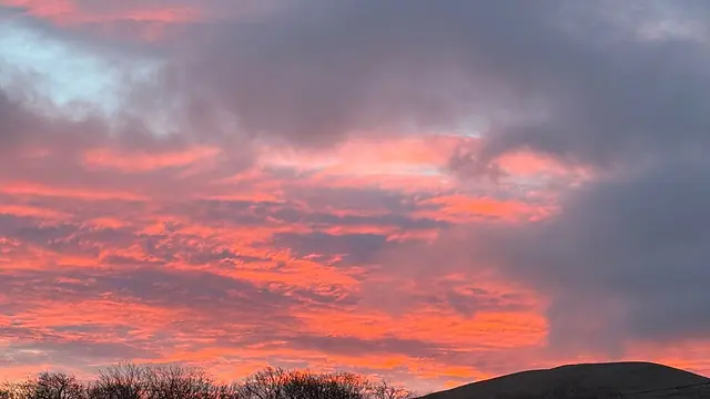 A red and pink sunset over the fell behind the holiday park at Lamplugh, with the caravans lit from inside.