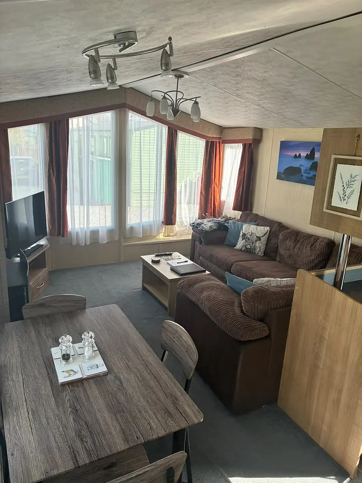The lounge in The Lake District Caravan with a brown corner sofa and blue cushions.