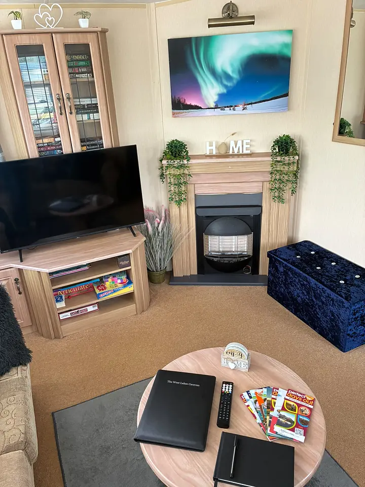 The lounge in The West Lakes Caravan with an electric fire and an aurora print above it.